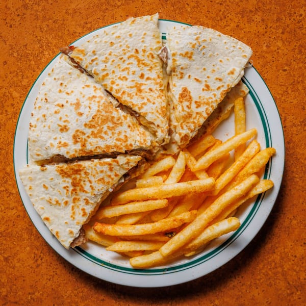 A plate of quesadilla slices with melted cheese and a side of seasoned french fries.